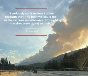 A car driving on a highway with a large plume of wildfire smoke in the sky ahead