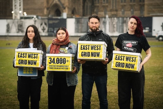 Four people holding signs that say "East West Grid Now"