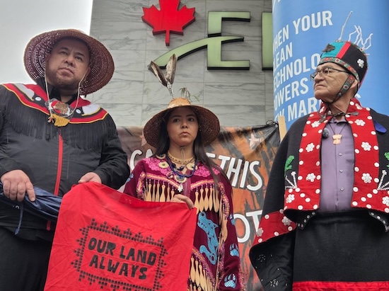 Three Indigenous people holding a small banner that says "Our land Always"